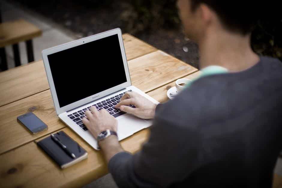 Mann schreibt mit Laptop auf einem Holztisch