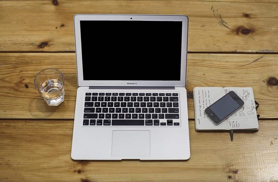 Macbook Air auf Holztisch - mit Glas Wasser, Notizblock und iPhone